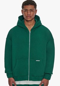 Dark green zippered hoodie made from soft material, featuring a large hood, front pockets, and ribbed cuffs. Simple design with no patterns.