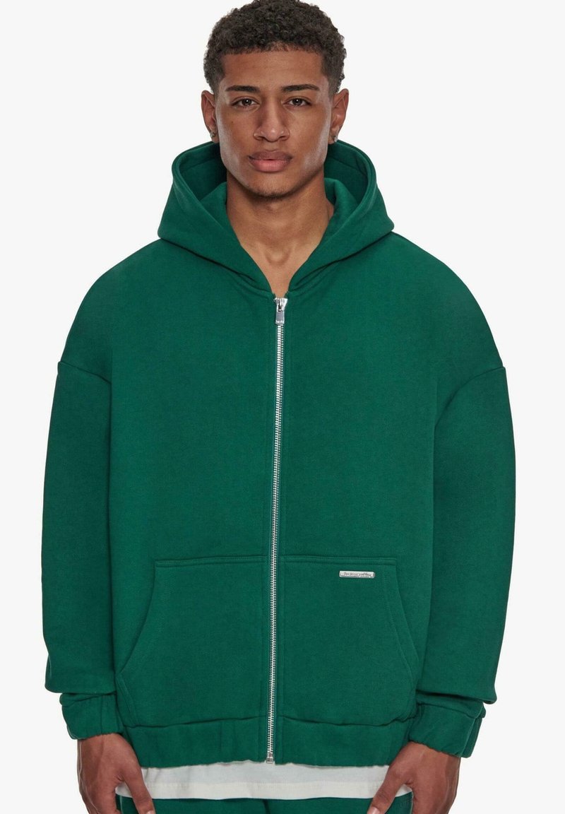 Dark green zippered hoodie made from soft material, featuring a large hood, front pockets, and ribbed cuffs. Simple design with no patterns.