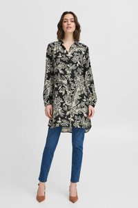 Abito camicia nero con motivo floreale in crema, dotato di maniche lunghe e chiusura con bottoni, abbinato a jeans blu e tacchi marroni.