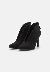 Scarpe nere in suede con tacco alto, punta affusolata, lati aperti e sottile tacco a stiletto. Presentano una chiusura con zip sul retro per una facile vestibilità.