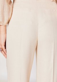 Pantaloni beige a gamba larga con un tessuto testurizzato, dettagli di cucitura sottili e due tasche posteriori, caratterizzati da un design a vita alta su misura.