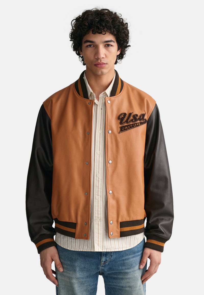 Braune und schwarze Collegejacke aus Leder und Stoffmaterialien, mit geripptem Kragen, Druckknöpfen und gesticktem "USA"-Detail.