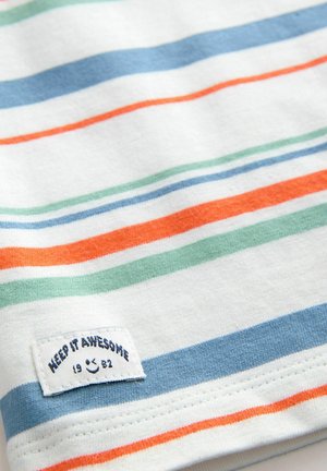 Witte stof met horizontale strepen in blauw, oranje en groen. Bevat een gestikt etiket met de tekst "HOU HET GAAN 1982."