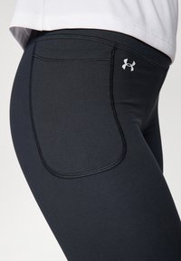 Leggings sportive neri con una texture liscia, cuciture decorative e una tasca laterale. Accento del logo in bianco sulla vita.