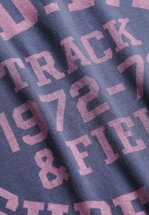 Mørkeblå T-shirt med stor lyserød tekst, der lyder "TRACK & FIELD 1972-73." Stoffet virker som bomuld med en blød, struktureret overflade.