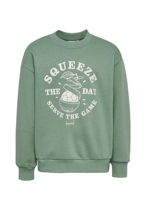 Grøn crewneck-sweatshirt med hvidt billede af en skrællet appelsin, der afslører en fodbold, og teksten "Pres dagen, tjen spillet."