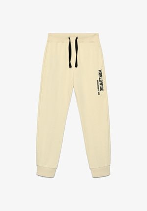 Pantaloni della tuta beige con una texture morbida, vita elastica, coulisse nere e una stampa laterale con la scritta "WORLDWIDE ESTABLISHED BY 1998."