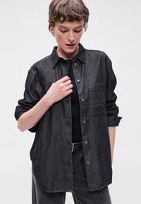 Μαύρο τζιν πουκάμισο με σχέδιο που κλείνει με κουμπιά, μία τσέπη στο στήθος και κουμπωμένα μανίκια. Λείος υλικός ιστός με χαλαρή εφαρμογή.