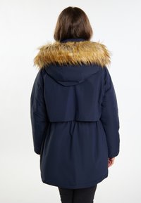 Mørkeblå pufferjakke med falsk pelskrave, indsnævret talje og hætte. Glat tekstur med lange ærmer og knælangt design.