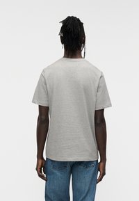 Γκρι βαμβακερό t-shirt με στρογγυλή λαιμόκοψη και κοντά μανίκια, με άνετη εφαρμογή. Η πίσω όψη εμφανίζει ομαλή υφή και απλό σχέδιο.