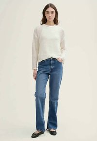 Suéter texturizado en color blanco roto con mangas largas, combinado con jeans de campana azul medio. Zapatos planos negros completan el look.