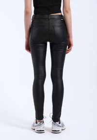 Czarne legginsy z ekoskóry o zwężanym kroju, z tylnymi kieszeniami i gładką, błyszczącą fakturą. Połączone z szarymi butami sportowymi.