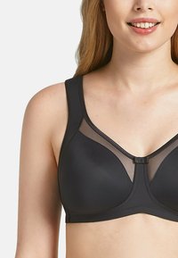Black bra with a smooth fabric, sheer mesh panel details, wide straps, and a central clasp. Designed in a structured, supportive shape.
