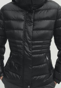 Sort dunjakke med en blank finish, med lynlås foran, to sidelommer og en tætsiddende hætte designet til varme.