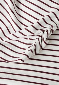 Biała tkanina z bordowymi poziomymi paskami, o miękkiej, gładkiej fakturze i marszczonym detalu na krawędzi.