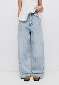 Lichtblauwe wijde jeans van denim, met een hoge taille, subtiele vervaging en gestikte details, gecombineerd met een paar tan schoenen.