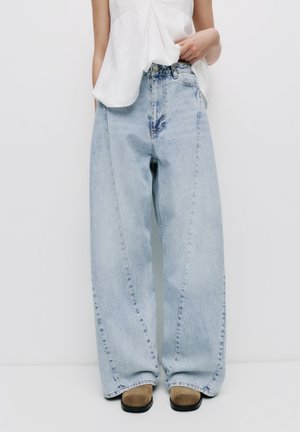 Light blue wide-legged jeans made of denim, featuring a high waist, subtle fading, and stitched detailing, paired with tan shoes.