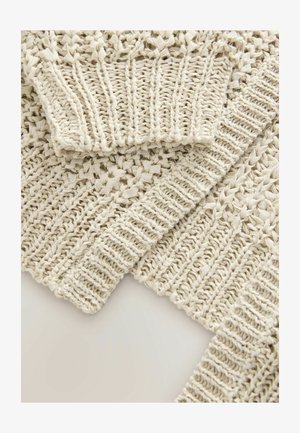 Beige stickad tyg med intrikata öppna vävningar och texturerade ribbade kanter. Har ett mjukt, lätt utseende med detaljerade mönster.