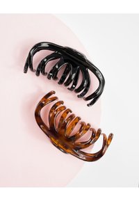 Due clip per capelli: una in plastica nera lucida e l'altra in tartaruga, entrambe con artigli curvi e allungati, posate su una superficie rosa.