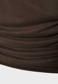 Gros plan d'un tissu brun foncé avec des plis horizontaux doux et une couture visible le long du bord.