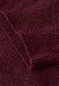 Pull en tricot bourgogne avec une texture douce, doté de poignets côtelés et d'un col plat, présentant des variations subtiles de couleur.
