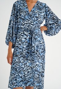 Blå och svart mönstrad klänning med långa puffärmar, ett knyt i midjan och en djup V-ringning. Lätt tyg med lätt lyster.