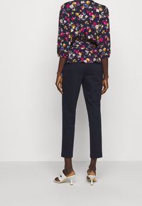 Blusa floreale in blu navy con maniche a sbuffo corte, decorata con fiori multicolori. Abbinata a pantaloni attillati scuri e sandali con tacco bianchi.