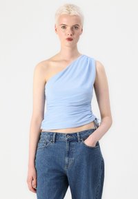 Lichtblauw top met één schouder van rekbaar materiaal, voorzien van geplooide details ter hoogte van de taille, gecombineerd met high-waisted, donkerblauwe spijkerbroek.
