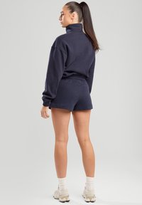 Navy blue cotton sweatshirt with a high collar, paired with matching shorts. Features a relaxed fit and soft texture. Light footwear completes the look.
