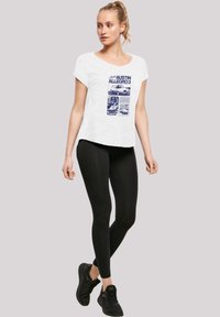 Weißes Kurzarm-T-Shirt mit blauem Grafikdruck, kombiniert mit schwarzen Leggings und schwarzen Sportschuhen. Schlicht, lässige Passform.