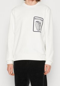 Vit sweatshirt med en svart bärillustration och textdesign med "Marc O'Polo" på fickan. Ribbstickade muddar och nederkant, mjuk tygstruktur.