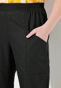 Svarta linnebyxor med en avslappnad passform, försedd med ett elastiskt midjeband och sidfickor. Tygkvaliteten har en slät yta och en minimalistisk design.