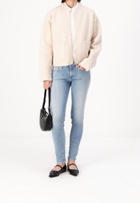 Beige fleece bomberjacka med två framfickor, tillsammans med ljusblå smala jeans och svarta lägenheter med hålmönster.