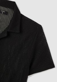 Polo nera a maniche corte con design a maglia testurizzata, colletto classico e piccola etichetta all'interno.