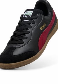 Črne usnjene in semiš superge z maroon poudarki, strukturirano gumijasto podplato, ravnimi črnimi vezalkami in zlate podrobnosti z logotipom "KING". PUMA blagovna znamka na jeziku.
