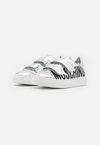 Sneakers sintetiche argento con doppie cinghie in Velcro, dotate di un logo nero "Moschino" sul lato e suola in gomma bianca.