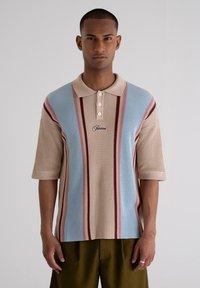 Knit polo shirt featuring a beige base with blue and red vertical stripes, three-button placket, and an embroidered logo on the chest.