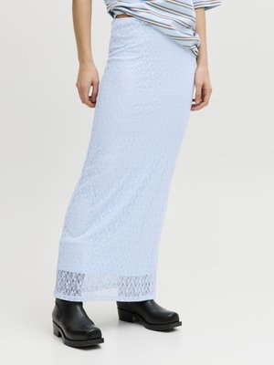 Femme portant une longue jupe en dentelle bleu clair associée à des bottines noires et une chemise rayée rentrée.