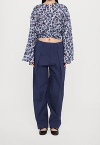 Blouse fluide à motif floral bleu et noir avec manches évasées, associée à un pantalon taille haute bleu marine avec plis sur le devant.