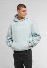 Felpa di colore azzurro chiaro realizzata in tessuto morbido, con tasca a marsupio e testo del logo bianco sul davanti. Abbinata a jeans scuri.