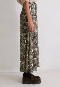 Jupe maxi vert foncé avec un grand imprimé floral crème. Le tissu tombe en douceur, présentant une taille haute. Assortie avec des chaussures slip-on marron.