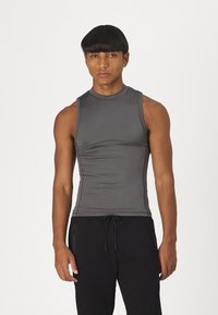 Haut sans manches gris en tissu extensible. Présente un col haut et une coupe ajustée, associé à un pantalon noir avec cordon de serrage.