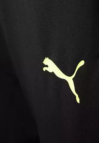 Un tessuto atletico nero presenta un evidente logo Puma giallo, che mostra il silhouette di un gatto in salto su uno sfondo uniforme.