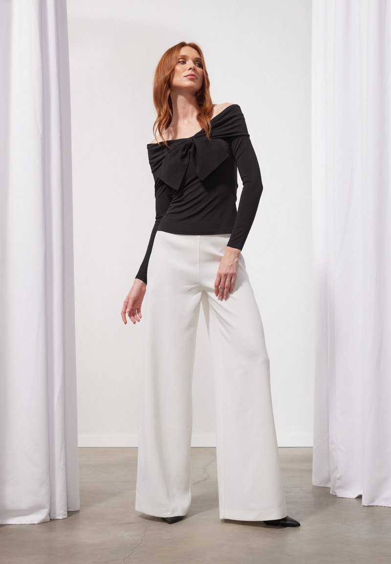 Schwarzes, schulterfreies Oberteil mit Schleifendetail, kombiniert mit weißen, weit geschnittenen Hosen. Glattes Material, klare Linien und taillierte Silhouette.