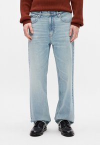 Gaiši zili džinsi ar taisnu piegriezumu, izbalējušu tekstūru, piecu kabatu dizainu un metāla furnitūru. Valkāti ar melnām kurpēm.