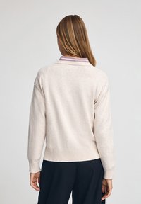 Beżowy sweter o miękkiej fakturze, z prążkowanym wykończeniem u dołu i na mankietach. Posiada różowo-białą, w paski kołnierz oraz luźny krój.