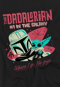 Black t-shirt featuring a graphic of a helmeted figure and a small creature. Text reads "THE DADALORIAN #1 IN THE GALAXY" with a retro design.