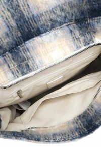 Tasche aus Wollfilz mit blauem und cremefarbenem Muster, ausgestattet mit einem beigen Stofffutter und einer metallischen Reißverschlusstasche innen. Strukturierte Außenseite und glatte Innenseite.