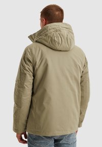 Ljus khakifärgad vadderad jacka med stor huva, quiltad design på huvan och sidofickor. Mjuk textur med avslappnad passform.