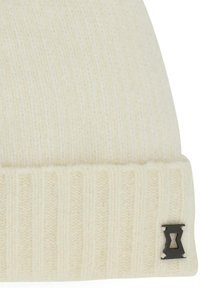 Crème gebreide beanie met een omgeplooide ribbelboord en een klein zwart metalen logo-accent aan de zijkant. Zachte textuur met een dikke weving.